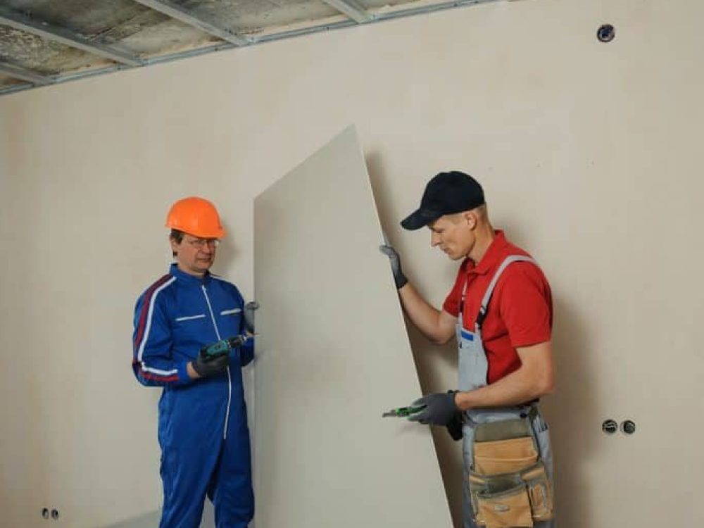 Contractors fitting drywall panel in residential hallway